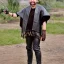 Placeholder: a young man wearing leather pants, a dirty mexico-themed poncho with a bowl cut and light facial hair, full body shot, holding 2 daggers with a smile