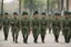 Placeholder: caucasian soldiers; marching in formation; facing away from camera; military parade; tight formation; shoulder to shoulder; marching along a street; green uniforms; medals and insignia; weapons in hands;