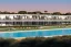 Placeholder: Sunset algarve in quinta do lago, a futuristic straight line luxury villa apartments with 250 meters long and a pool, overhang straight line terraces with black metallic beams and wood pergolas, with a separate clubhouse building facility with green roofs, overlooking the campus sport facility and inserted in the Ria Formosa Natural park, on a slope with pinus pinea, a wrap around low speed veicular road