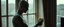 Placeholder: A photorealistic cinematic gothic horror scene of an extremely pale, sickly vampire quietly cleaning a large window in an ordinary old apartment during early morning. The vampire is doing the mundane task with calm, almost routine concentration, holding a worn cloth in one hand and a small spray bottle in the other. His skin is the main visual focus: extremely pale and unhealthy-looking, dry and uneven, with a naturally irregular organic texture, tiny pores, fine wrinkles, subtle flaky patches,