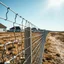 Placeholder: Photograph, wasteland, noon-light, huge fence in the background, bright, daylight, details of the powder very accentuated, high contrasts, fence, powder, aluminum, row of houses, glossy, organic, strong texture, fiotti.