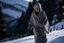 Placeholder: Una mujer mayor con la cara borrosa y mirada lateral, vestida con un camisón, camina sobre la nieve en un paraje de alta montaña. Fotografía con cámara Leica y objetivo de 35 mm