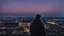 Placeholder: An Englishman in a bomber jacket standing to one side of a tall building looking across a city after sunset