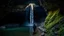 Placeholder: Interior of a large, natural cave. A tall waterfall cascades down one side, illuminated by a shaft of sunlight from above.a hooded figure is walking on a rocky path within the cave, further back from the waterfall, in a more dimly lit area. The path winds through the cave. Moss and other vegetation grow on the cave walls. Water pools below the waterfall. Photorealistic, 8k resolution, highly detailed, dramatic lighting, volumetric lighting