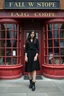 Placeholder: Photorealistic image of a young woman with dark hair, in a black ankle length skirt, boots and shirt, standing outside an old magic shop front with large red painted multi-paned picture windows on either side of a multi-paned doorway.