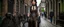 Placeholder: full-height portrait of a woman with straight shoulder-length black hair, with metal arms and legs, dressed in leather trousers, and a waistcoat, in a Victorian street next to a steampunk bike