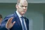 Placeholder: side view of Olaf Scholz walking, concerned expression, waving hand, pressed lips; in the style of VanGogh