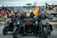 Placeholder: a very hard and tuff motorcycle young gang with Keltic hair , not old, posing with their Harley Davidsson bikes, some of them holding guns and shotguns, a logo sign with "FALKÖPING HD", "FEARLESS SINNERS" Skulls and bones, skeletons and fire, Swedish town Falköping in background, Swedish flags on bikes, Simon Stålenhag style
