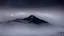 Placeholder: looking down from above at misty foreground and night sky, no sun, single sharp narrow mountain peak coming through the mist in the center