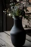Placeholder: detail image of an old black ceramic vase with flowers on a wooden table. modern farmhouse style with rustic feeling.