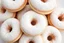 Placeholder: A close-up image of a pile of evenly powdered cake donuts, with the donuts overlapping and the powdered sugar coating them evenly. The background should be white or a light neutral color.