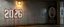 Placeholder: background of firing squad execution wall(wet textured concrete, gray, old, cracked, billet holes, blood stained, 1 wall light) from underground parking, german style, a large blocky upside down "2026" painted on left(old faded paint, red stains running down and past), cyberpunk, to the right a larger mural of a hung dead man, Republic of Gilead