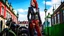 Placeholder: full-height portrait of a woman with straight shoulder-length auburn hair, with metal arms and legs, dressed in leather trousers, and a waistcoat, in a Victorian street next to a steampunk motorbike, blue sky