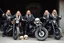 Placeholder: a very hard and tuff motorcycle young gang with long blond viking hair, not old, posing with their Harley Davidsson bikes, some of them holding guns and shotguns, a logo sign with Falköpings HD Club, "Fearless sinners" Skulls and bones, skeletons