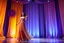 Placeholder: modern stage with gray-dark yellow blueish violet theme artistic decoration , color full dynamic lighting, a beautiful lady in maxi dress with shining silver jewels ,curvy long hair,dancing, 3D recursive fractal structure animating background