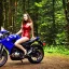 Placeholder: Very attractive woman sitting on a motorcycle. The bike is Yamaha. In the background is a forest.