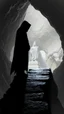 Placeholder: A hooded creature shadow standing on a narrow black stone path above the ground in a cave which has a big god statute
