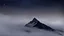 Placeholder: misty foreground and night sky background, no sun, single sharp narrow mountain peak coming through the mist in the center