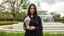 Placeholder: Hyper Realistic Photographic Front View Of A Beautiful Young Pakistani Pashto Woman (With Beautiful Long Black Hair) Wearing A Beautiful Black Dress With Black Embroidery And Black Dupatta; Happily Holding A White Pigeon And Standing With Green Grass With A White Marble Water Fountain Behind Her At Beautiful Cloudy Day Showing Dramatic And Cinematic Ambiance.