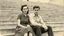 Placeholder: retro monochrome photo of a young hungarian couple in 60s style outfit sitting on the stone stairs in Budapest , the photo is old, stained and scratched in some places, one corner of the photo is missing, the girl's and the boy's faces not clearly visible, blured, behind them are many stairs, summer, moody photo
