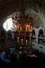 Placeholder: in the art style of Karem Beyit: a chandelier of bones above a table of candles, holders and snuffers. bowls of charcoal. A catacomb of burial niches in the background