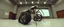 Placeholder: in the style of Escher and Giger and Fallout 4, pinhole cam, airbrush 3d rendering, on tv screen:A five-second cinematic single take in a clean industrial presentation hall. A bizarre mechanically plausible tracked atv machine stands beside a presentation podium, designed to look like a giant mechanical praying mantis. Two large bicycle wheels form its main body and four thin articulated mechanical legs support it. Two long folded mechanical front arms resemble mantis forelegs, huge head and arm