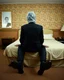 Placeholder: man with plastic bag over his head sits on the edge of a bed with his feet on the ground, facing camera, inside an old, 70s style motel room with tacky wall paper. he is wearing a black suit with a melincholy attitude. there is a box tv facing away from camera, illuminating his front. from this view, you cannot see the front of the tv. full room view, super wide shot, 24mm lens view, film syle.