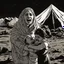 Placeholder: A Palestinian woman wearing the Palestinian dress carries her dead son as she screams and cries at night, with explosions in refugee tents behind her.