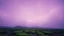 Placeholder: The sky is a bleached violet with light smoke. Below, the desolate mesa is covered with lush moss. In the distance, there are cottages.