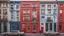 Placeholder: A building with a vibrant red and blue facade featuring several windows with white frames and one window with a partially drawn curtain, surrounded by a bustling city street