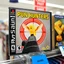 Placeholder: close up on a Playstation video game case on display on a store shelf for game titled "PUN HUNTERS", game case image is a pixelated video game image of a red sniper crosshair zeroing in on an anthropomorphic butter stick with wings, rated M for mature, original playstation game box satire,