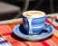 Placeholder: Cappuccino art microfoam in blue mug saucer Crawford plaid napkin Demitasse