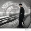 Placeholder: A young Asian man with long hair and a black trench coat waiting for a woman at a train station in Tokyo