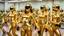 Placeholder: Hyperrealistisch dutzende Rollergirls völlig verhüllt von golden glänzendem Ganzkörper-Zentai mit geschlossenem verspiegelten Visier in identischen goldfarbenen, geschlossenen Helmen fahren in präziser Formation parallel nebeneinander und hintereinander mit Rollschuhen