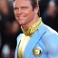 Placeholder: A superhero man with a sky blue spandex suit. He has a sky blue mask on, blue eyes, freckles, dimples, and curly dark brown hair. He's wearing gold boots and gold artist gloves with a white belt and has a gold M on his chest. His boots have small feathered wings on them, and his shoulders have shoulder pads. He is smiling