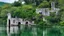 Placeholder: A ruined stone building in a lake, balconies, verandas, arches, bridges, spires, stairs, trees, dense foliage, spanish moss, ivy, blue sky, white clouds