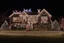 Placeholder: photograph taken by a drone gopro camera of a large suburban house and landscaping and fence with an insanely detailed Christmas light display lit up at night. Christmas lights on everything, Santa's sleigh and reindeer on roof all lit up with individual christmas lights, christmas light on everything to an unbelievable degree, 100,000 individual lights, ridiculous and impossible amount of lights, lights can be seen from space