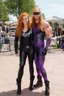 Placeholder: Debby Ryan, smiling, Heavy Metal t-shirt, Black Leather biker's jacket, Black leather pants, Platform boots, midday, bright sunlight, extremely colorful. Big, fluffy hair, Debby Ryan has Auburn Red hair, green eyes, She is standing next to ((THE PHANTOM, an extremely muscular man who wears a one-piece, formfitting purple body suit with tribal designs lightly woven into the fabric. He also wears a cowl, eye mask, black boots, black gloves, double holstered pistol belt