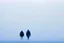 Placeholder: two people seen from behind walking side by side in an empty foggy plain, above there is blue sky