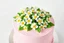 Placeholder: A beautifully decorated cake with pink frosting and an array of meticulously crafted white flowers with yellow centers on top. The flowers are surrounded by green leaves, creating a vibrant and appealing presentation against a light background.on white background