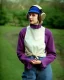 Placeholder: Everything she wear is in the image. of young woman, plum-blue-magenta-camouflage. She wears mantel and simple blouse.Felt cloth visor with tippet. SMALL FELT CAP is merged to Old AKG headphones with recognizable Golden rings! cloth materials are denim and felt cloth mixed. Fashion 1990's. Colors: Cream white, zinc plate, red ochre, ochre, orange - all mixed. Thick tights. Thick calves. She is in figure from top to toe.