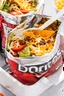 Placeholder: "Taco in a Bag" which consists of an open Doritos chip bag with sides rolled down, containing Doritos chips and cooked ground beef and lettuce and shredded cheese and chopped tomato pepper and onions and topped with more nacho chips, plastic fork, food blogger photography