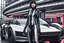 Placeholder: A Full-Length Pale Dark-Haired Woman With A Straight Bob Hairstyle With A Fringe, In A Futuristic Leather Outfit, And Gloves, Standing Next To A Futuristic Car, in a futuristic city