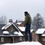 Placeholder: in the North of Canada, among neighbors in a small group of houses, an Afro-American man stands on the edge of the roof just before a snowstorm hits. He attaches plank plates to the roof to reinforce it, bracing for the impending storm. The cold air bites at his skin, the wind howling ominously, as he works diligently to secure the roof against the fury of the upcoming blizzard.
