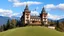 Placeholder: a large, ornate castle with two towers on top of a hill. The castle is made of wood and has multiple levels with intricate details. The towers have pointed spires and a flagpole with a flag flying in the center. The building is surrounded by trees and shrubs, and there is a grassy hill in front of it. The sky is blue with white clouds, and the mountains can be seen in the background. The overall atmosphere is peaceful and serene.
