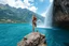 Placeholder: a picture of natural landscape that includes majestic mountains and a serene countryside. Additionally, incorporate details about a stunning, large waterfall that enhances the beauty of the scene. The output should be structured as a narrative, painting a clear image with rich, descriptive language that evokes the sights and sounds of this beautiful environment water fall falls to a big sea with modern ship in it.a fullbody lady in One Piece - Athletic Swimsuit,standing over a rock at hight
