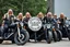 Placeholder: a very hard and tuff motorcycle young gang with long blond viking hair, not old, posing with their Harley Davidsson bikes, some of them holding guns and shotguns, a logo sign with Falköpings HD Club, "Fearless sinners" Skulls and bones, skeletons