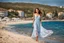 Placeholder: long shot, beautiful Turkish girl with nice blue eyes wearing a dress walks in shore toward camera , sharp focus all the scene, natural light, vertical composition, relaxed and natural, fresh and comfortable ,in seaside there are luxury beach hotels.