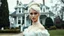 Placeholder: High resolution and sharp focus photo of an lovely and beautiful caucasian 19 year old woman. She has thick platinum hair worn in a chignon. She is dressed in a beautiful white victorian gown. She is standing in in front of a victorian house. She is looking at the viewer.