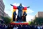 Placeholder: 200 ft tall cartoonish jesus parade balloon pulled by multiple grim reapers, multi colored, bright, vivid, psychedelic, high detailed, high gloss, insanely detailed, matte, horrorcore, lining the street, unsettling contrast, monument to death, live action shot grim reaper parade, pulling a jesus parade float